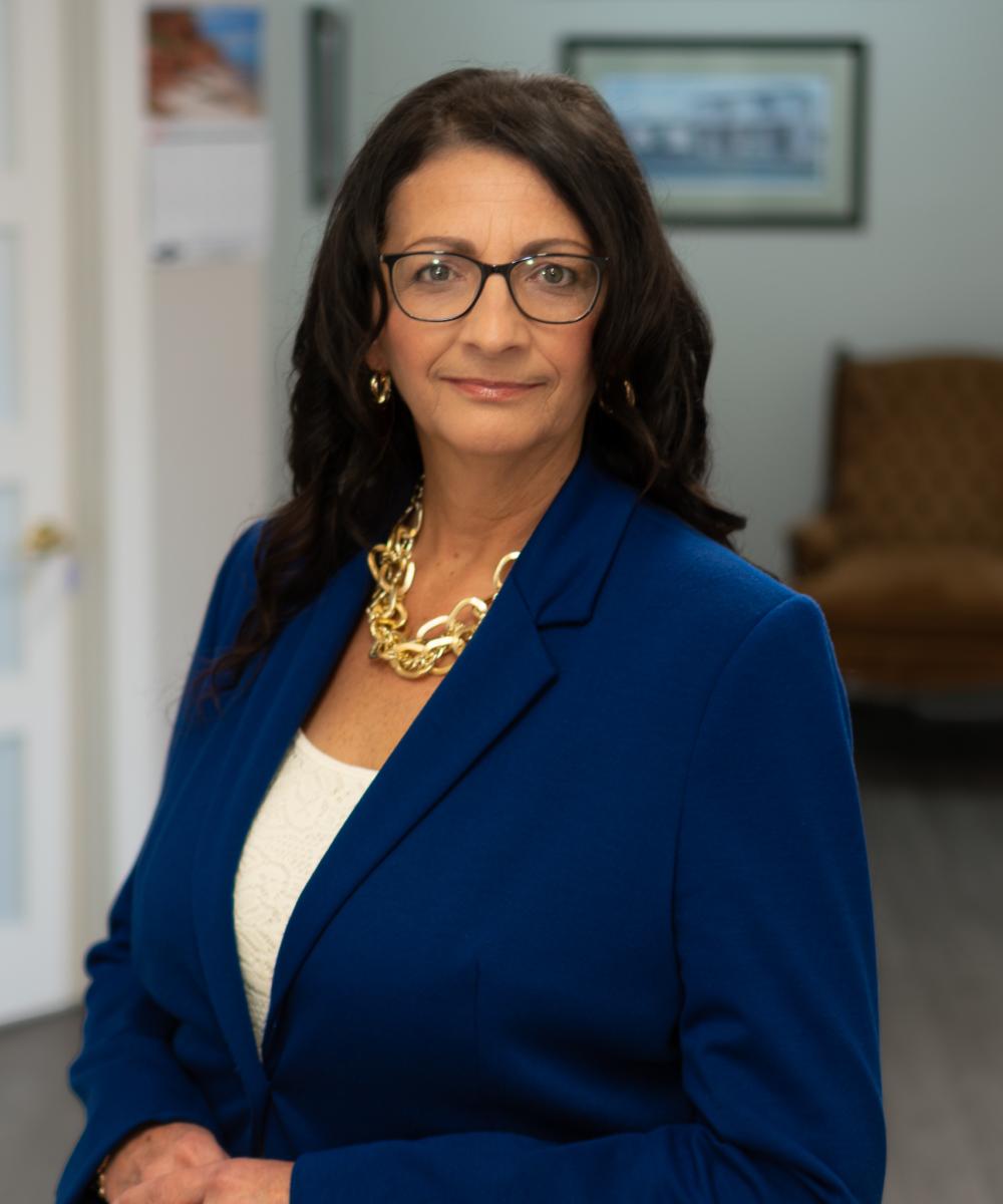 Dawn Lynch, Executive Assistant at Dawson & Associates IG Private Wealth Management, wearing glasses, a blue blazer, and a gold necklace in a professional office portrait.